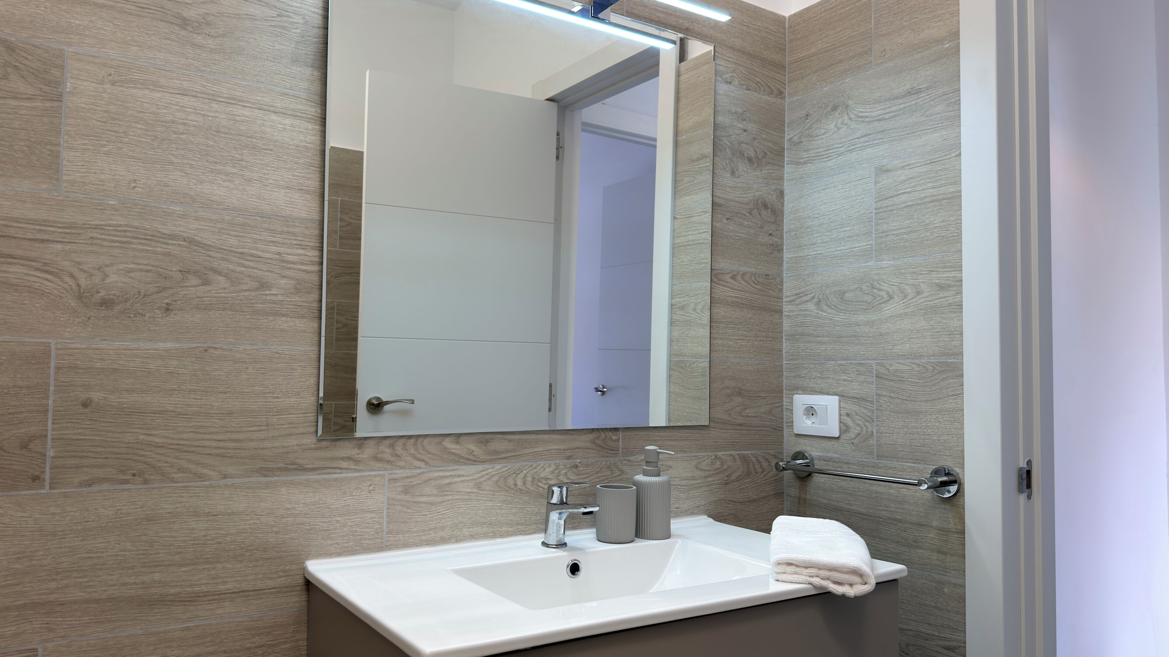 A modern bathroom with a white sink, mirror, and towel rack.