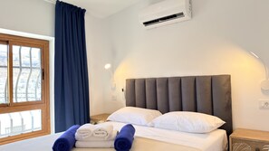 Ein Hotelzimmer mit Bett, Fenster mit Vorhängen, Klimaanlage und Wandlampe.