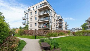 Een meerlaags woongebouw met balkons, een geplaveid pad en een gazon met beplanting.