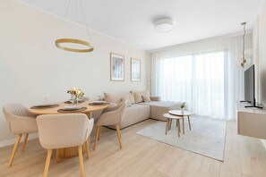 Ein modernes Wohnzimmer mit einer Couch, einem Esstisch, Stühlen, einem Fernseher und Kunstwerken an der Wand.