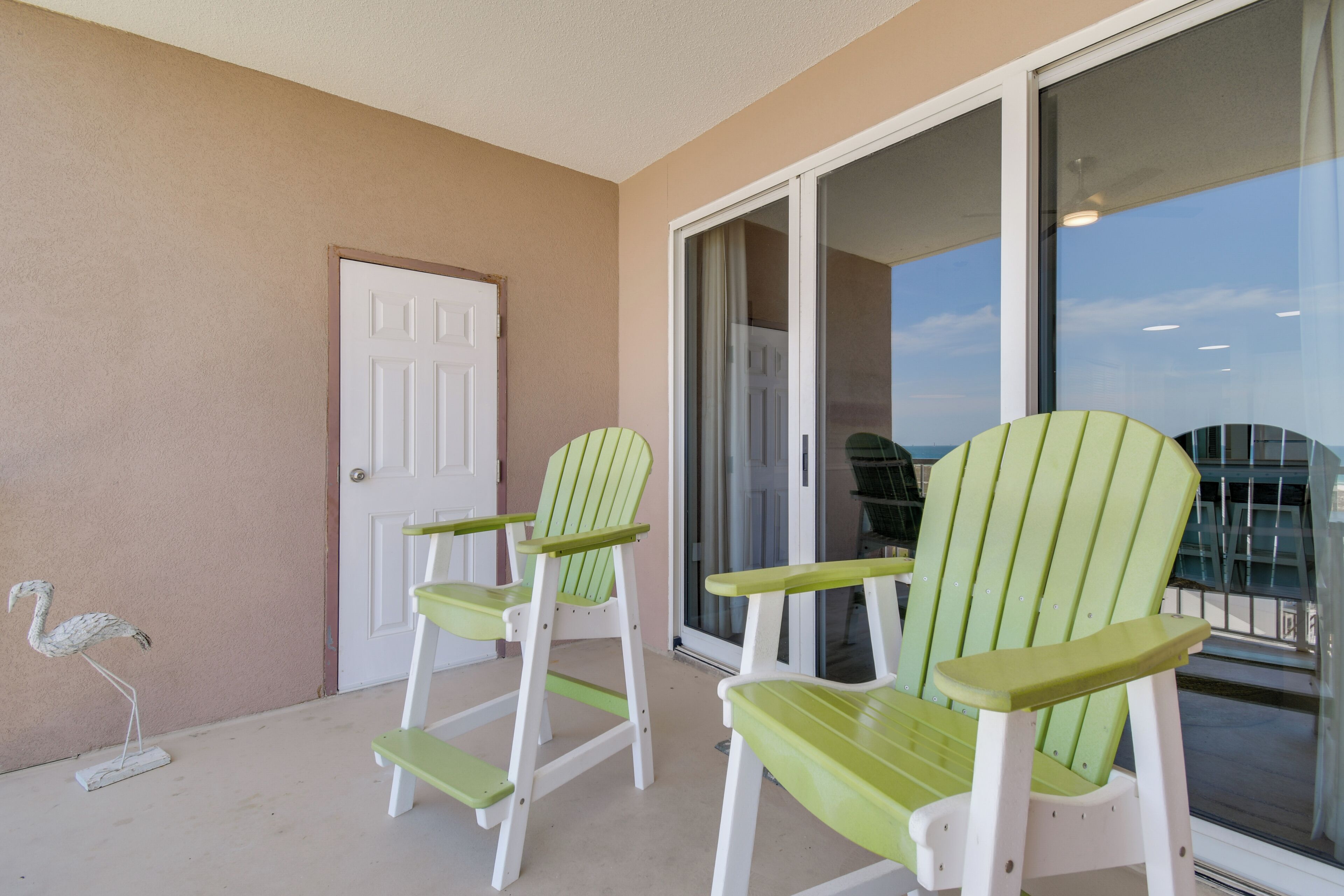A balcony with two green Adirondack chairs, a white door, and a glass door leading to a balcony.