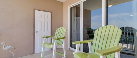 A balcony with two green Adirondack chairs, a white door, and a glass door leading to a balcony.