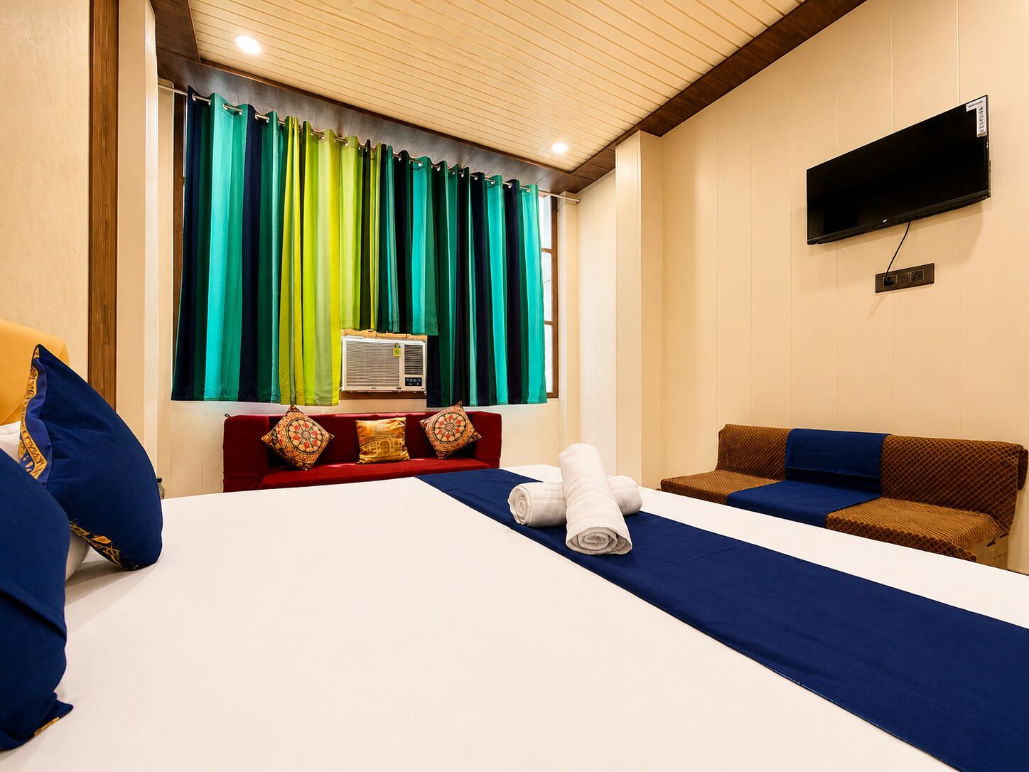 Habitació d'hotel amb llit, televisió i finestra amb cortines.