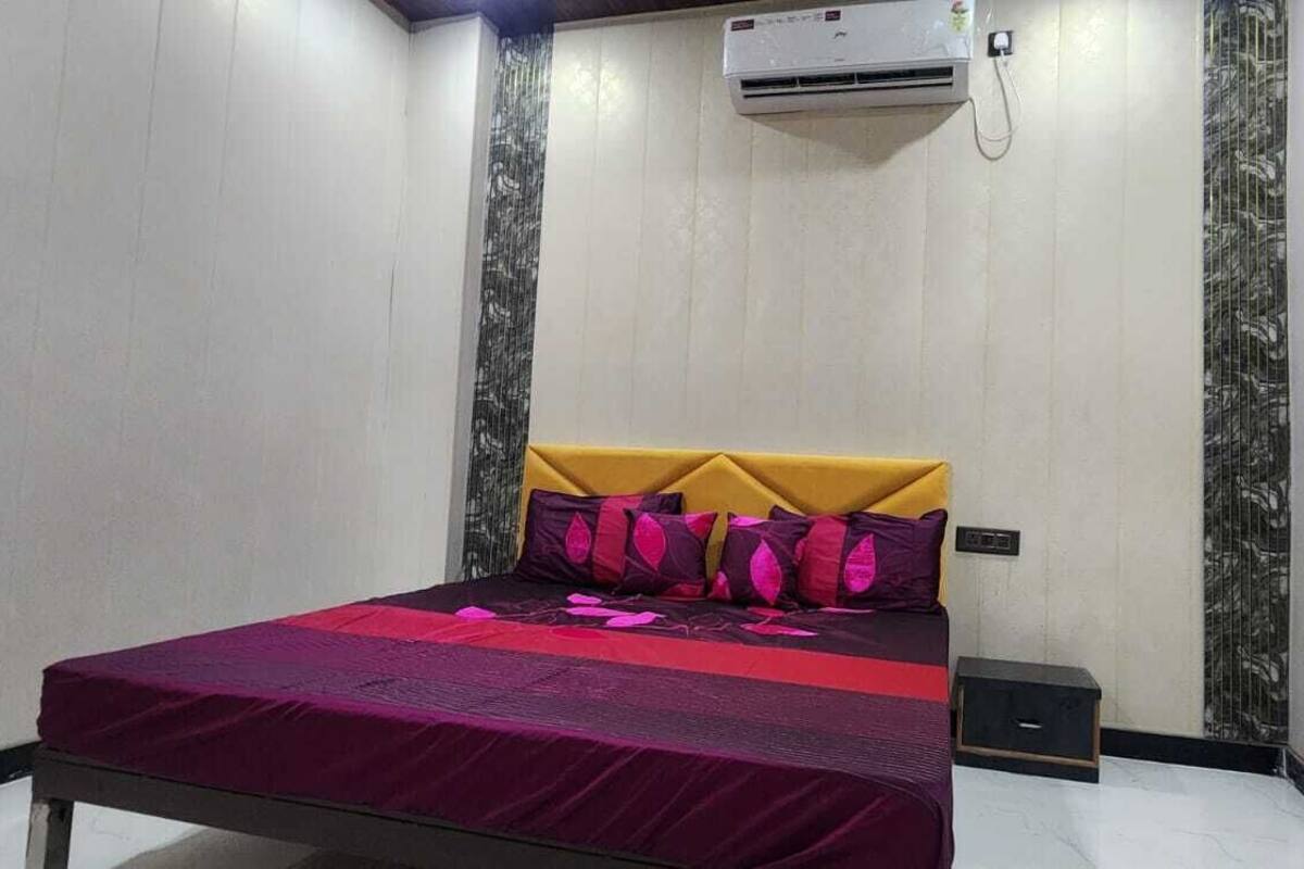 Quarto com cama, cabeceira, mesa de cabeceira, aparelho de ar condicionado e tomada na parede.