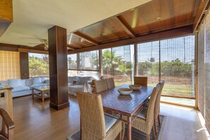 A spacious living area with a dining table, wicker chairs, a sofa, and a large window with a view of greenery. - Holiday Home 'Elegance, Privacy, and Comfort' with Sea View, Private Pool and Wi-Fi (Calafell)