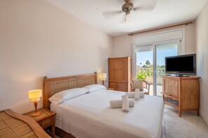 A hotel room with a bed, a television, a wooden wardrobe, a balcony with a view, and a ceiling fan. - Holiday Home 'Elegance, Privacy, and Comfort' with Sea View, Private Pool and Wi-Fi (Calafell)