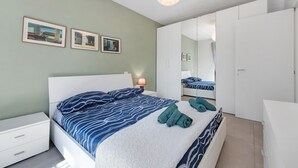 A bedroom with a bed, white nightstands, a bedside lamp, a wardrobe, and two framed pictures on the wall. - Apartment 'Caky's House' with Shared Terrace, Wi-Fi and Air Conditioning (Desenzano del Garda)