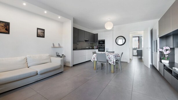 A modern living room with a sofa, dining table, and chairs, a kitchen with dark cabinets and a microwave, and a hallway leading to another room. - Apartment 'Caky's House' with Shared Terrace, Wi-Fi and Air Conditioning (Desenzano del Garda)