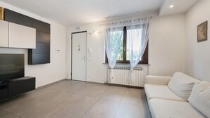 A modern living room with a flat-screen TV, a sofa, a door, and a window with sheer curtains. - Apartment 'Caky's House' with Shared Terrace, Wi-Fi and Air Conditioning (Desenzano del Garda)