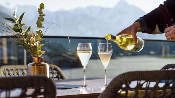 A table with two wine glasses, a bottle of wine being poured, and a vase with greenery. - Exclusive vacation apartments with private spa in the Tyrolean Alps (Zellbergeben)