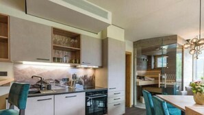 A modern kitchen with built-in appliances, a dining area with teal chairs, and a wooden dining table. - Exclusive vacation apartments with private spa in the Tyrolean Alps (Zellbergeben)