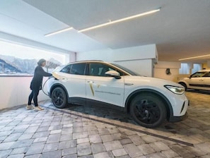 Ein weißer SUV steht in einer Garage mit gepflastertem Boden, neben ihm eine Person.
