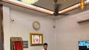 A reception desk with a clock, a framed artwork, and a television on the wall. - Hotel Kartik (Zirakpur)