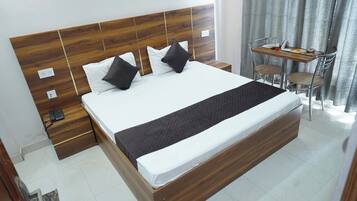 Una habitación de hotel con cabecera de madera, cama con ropa blanca, una manta de color negro y una pequeña mesa con sillas.
