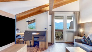 Een moderne kamer met een houten plafond, een eethoek, een bank en uitzicht op bergen door een glazen deur.