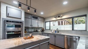 A modern kitchen with stainless steel appliances, a marble countertop, and a large window providing a view of the outside. - Luxury on Ocean Drive - Sleeps 28 (Corpus Christi)