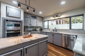 A modern kitchen with stainless steel appliances, a marble countertop, and a large window providing a view of the outside. - Luxury on Ocean Drive - Sleeps 28 (Corpus Christi)