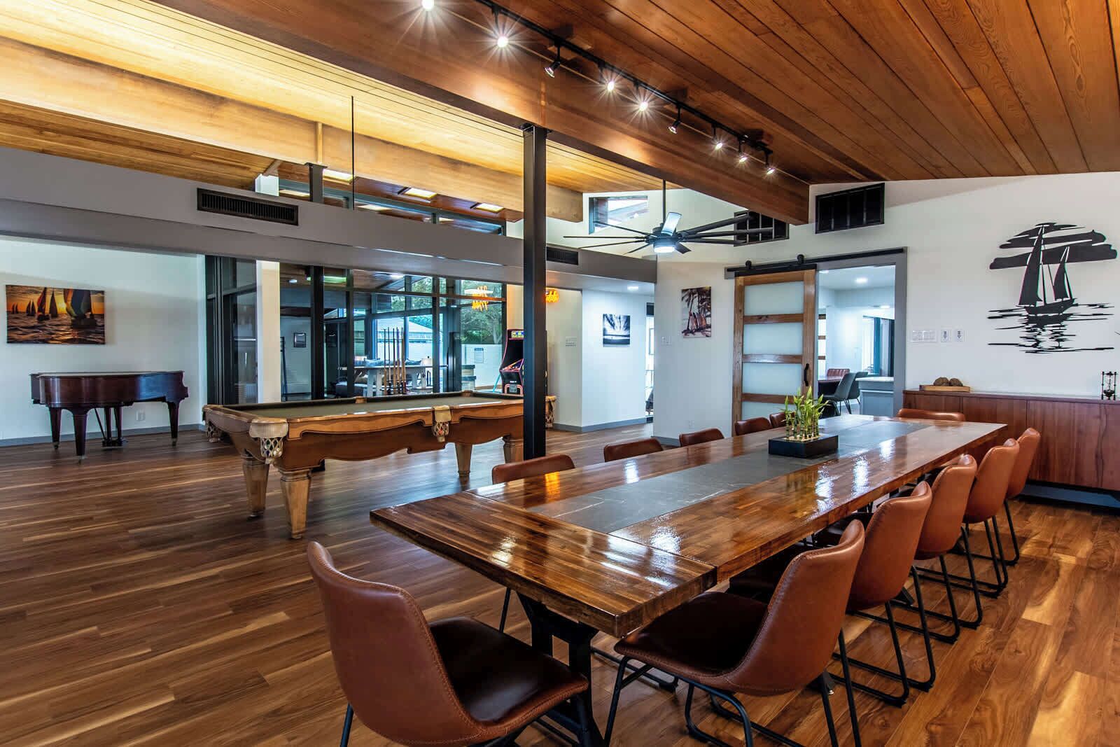 A spacious room with a long wooden table, brown leather chairs, a pool table, and a piano.