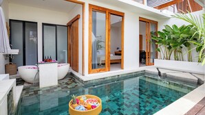 A modern pool area with a glass-bottomed pool, a large white bathtub, and a wicker basket with fruits and bottles. - Harmony Villas  (Denpasar)