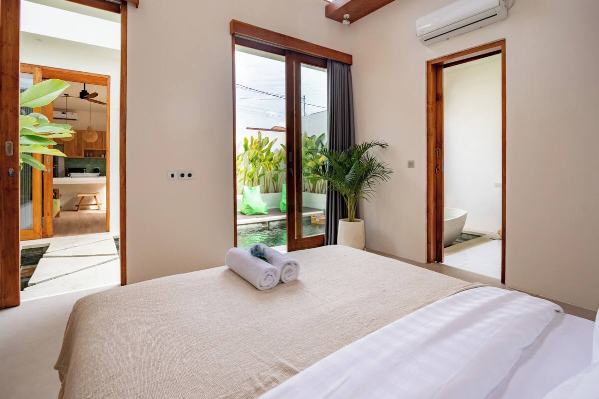 Un dormitorio con cama, una planta en maceta, baño y vistas a un balcón.