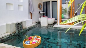 A swimming pool with a floating basket of fruits and a modern bathroom with a large bathtub and a round mirror. - Harmony Villas  (Denpasar)