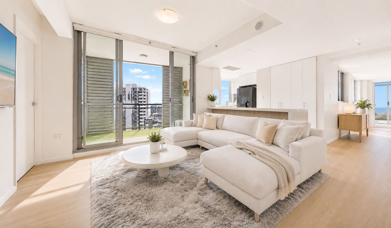 A modern living room with a sectional sofa, a round coffee table, and a view of the city through large sliding doors.