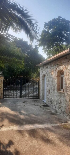 Edifici de pedra amb una petita finestra, una reixa de metall i una palmera al fons.