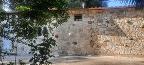 A stone wall with a small window and a door, surrounded by greenery. - Traditional Stone House in Kerkira Argyrades (Argyrades Kerkira)