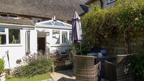 A patio with wicker furniture, a table, and a covered umbrella. - Honeypot Cottage (Weymouth)