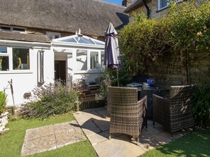A patio with wicker furniture, a table, and a covered umbrella. - Honeypot Cottage (Weymouth)