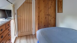 A bedroom with a bed, wooden wardrobe, and a television on a dresser. - Honeypot Cottage (Weymouth)