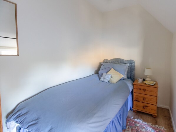 Ein Schlafzimmer mit einem Bett, einem Nachttisch, einer Lampe und einer kleinen Holzkommode.