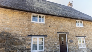 A stone building with a dark door, two windows with shutters, and a chimney. - Honeypot Cottage (Weymouth)