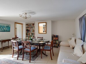 Ein Essbereich mit einem runden Tisch, Stühlen und einer Chandelier. An den Bücherregalen befinden sich Bücher und ein Gemälde an der Wand.