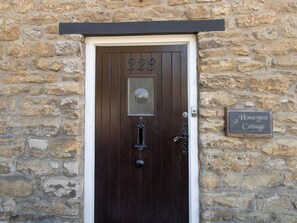 Eine Steinsäule mit einer Holztür, auf der '228' steht, und einem Schild mit der Aufschrift 'Honeypot Cottage'.