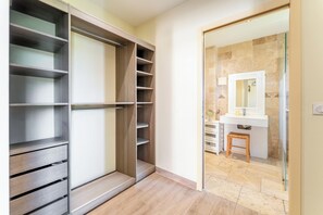 Un dressing avec de nombreuses étagères et des tiroirs, une salle de bain avec un lavabo et un miroir, et un tabouret en bois.