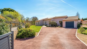 En boligkørevej der fører til et hus med garage, omgivet af grønt og en klar himmel.