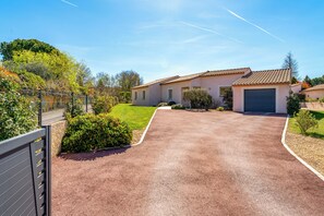 Une allée menant à une maison avec un garage, entourée de verdure et sous un ciel dégagé.