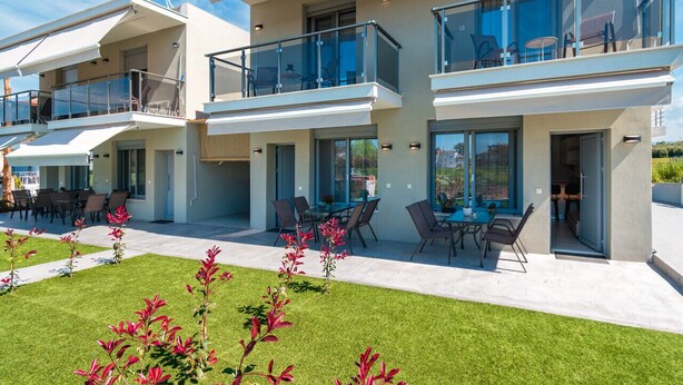 A modern multi-story residential building with balconies, outdoor seating, and a well-maintained lawn. - Stefanos Maisonettes by RentalsPro - Portaria Beach (Nea Moudania)