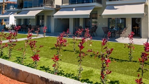 A modern multi-story hotel with balconies, outdoor seating, and a well-maintained lawn. - Stefanos Maisonettes by RentalsPro - Portaria Beach (Nea Moudania)