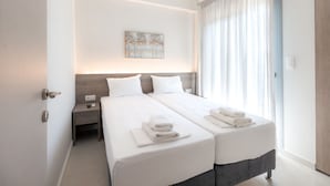 A hotel room with two beds, a nightstand, a painting on the wall, and a window with curtains. - Stefanos Maisonettes by RentalsPro - Portaria Beach (Nea Moudania)