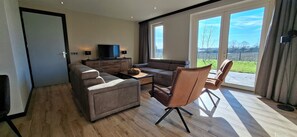 Uma sala de estar moderna com um sofá, poltrona e uma televisão sobre um móvel de madeira.