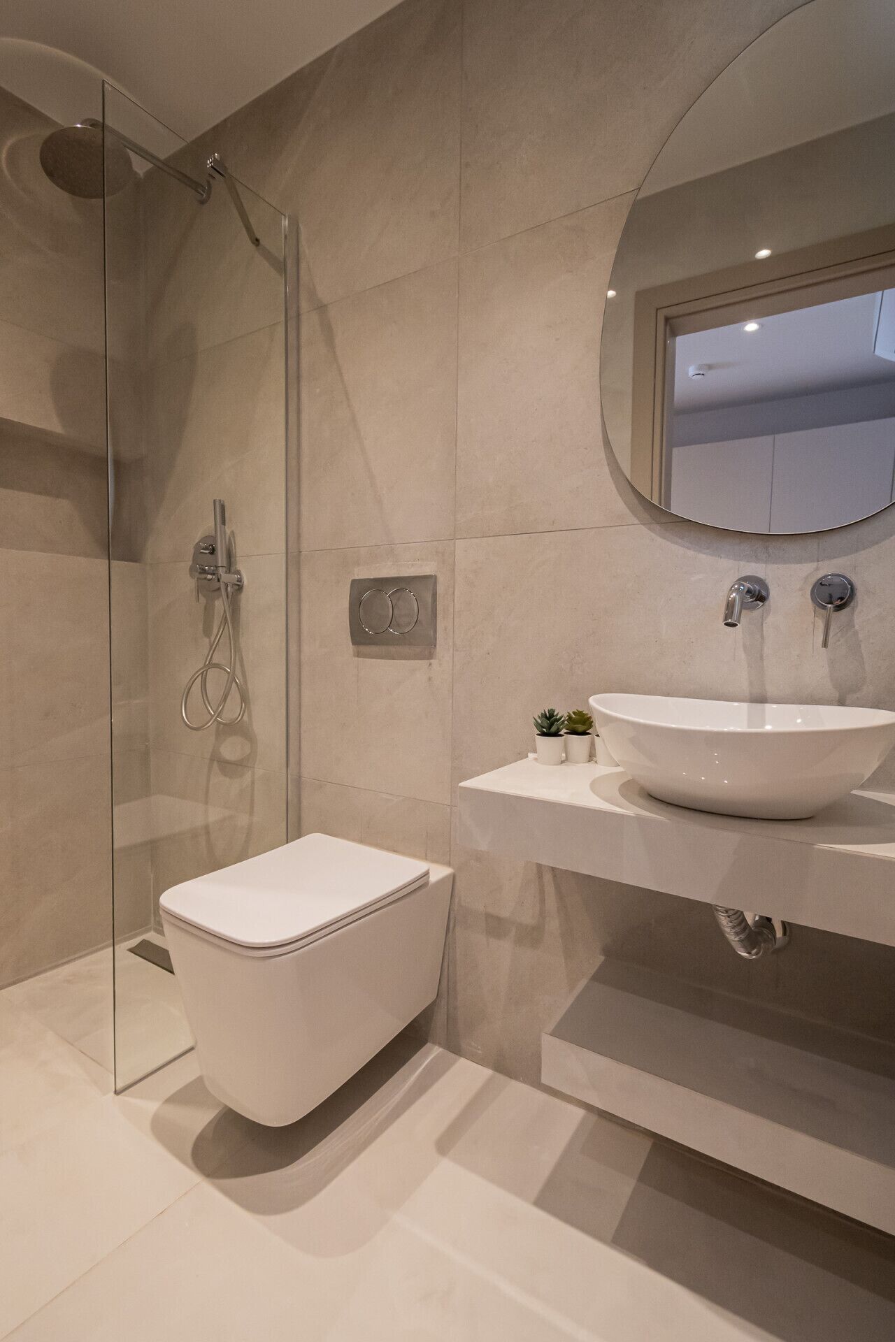 Een moderne badkamer met een douchecabine van glas, een wit toilet en een groot wastafelmeubel met een spiegel erboven.