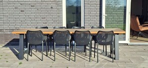 Un espacio de comedor al aire libre con pared de ladrillo, mesa de madera y sillas de malla negra.