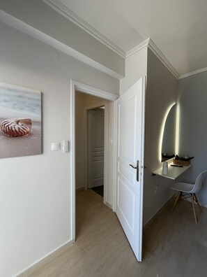 A hallway with a door leading to a room, a wall-mounted light, a chair, and a framed picture. - Cali-Waves Apartment by RentalsPro - Halkidiki (Poligiros)