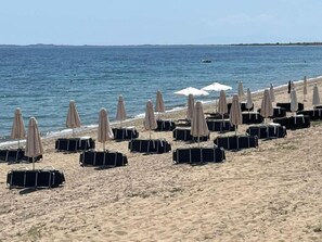 A beach with rows of black luggage and beige beach umbrellas. - Cali-Waves Apartment by RentalsPro - Halkidiki (Poligiros)