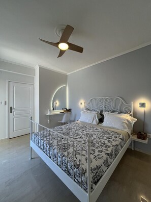 A bedroom with a bed, a ceiling fan, bedside lamps, a nightstand, and a door. - Cali-Waves Apartment by RentalsPro - Halkidiki (Poligiros)