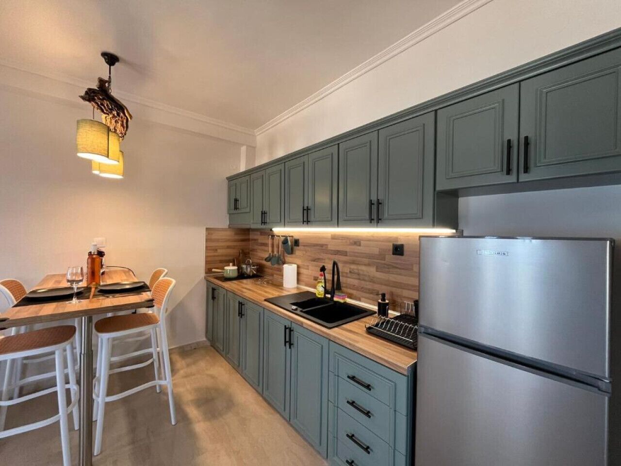 Una cocina moderna con armarios azul claro, un refrigerador de acero inoxidable, una encimera de madera y una lámpara colgante.