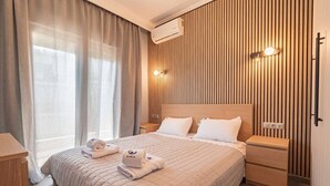 Ett hotellrum med en säng, sängbord, ett fönster med gardiner, en väggmonterad luftkonditioneringsanläggning och en vägg med vertikala träribbor.