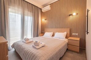 Ein Hotelzimmer mit Bett, Nachttischen, einem Fenster mit Vorhängen, einer Wandmontage-Klimaanlage und einer Wand mit vertikalen Holzleisten.